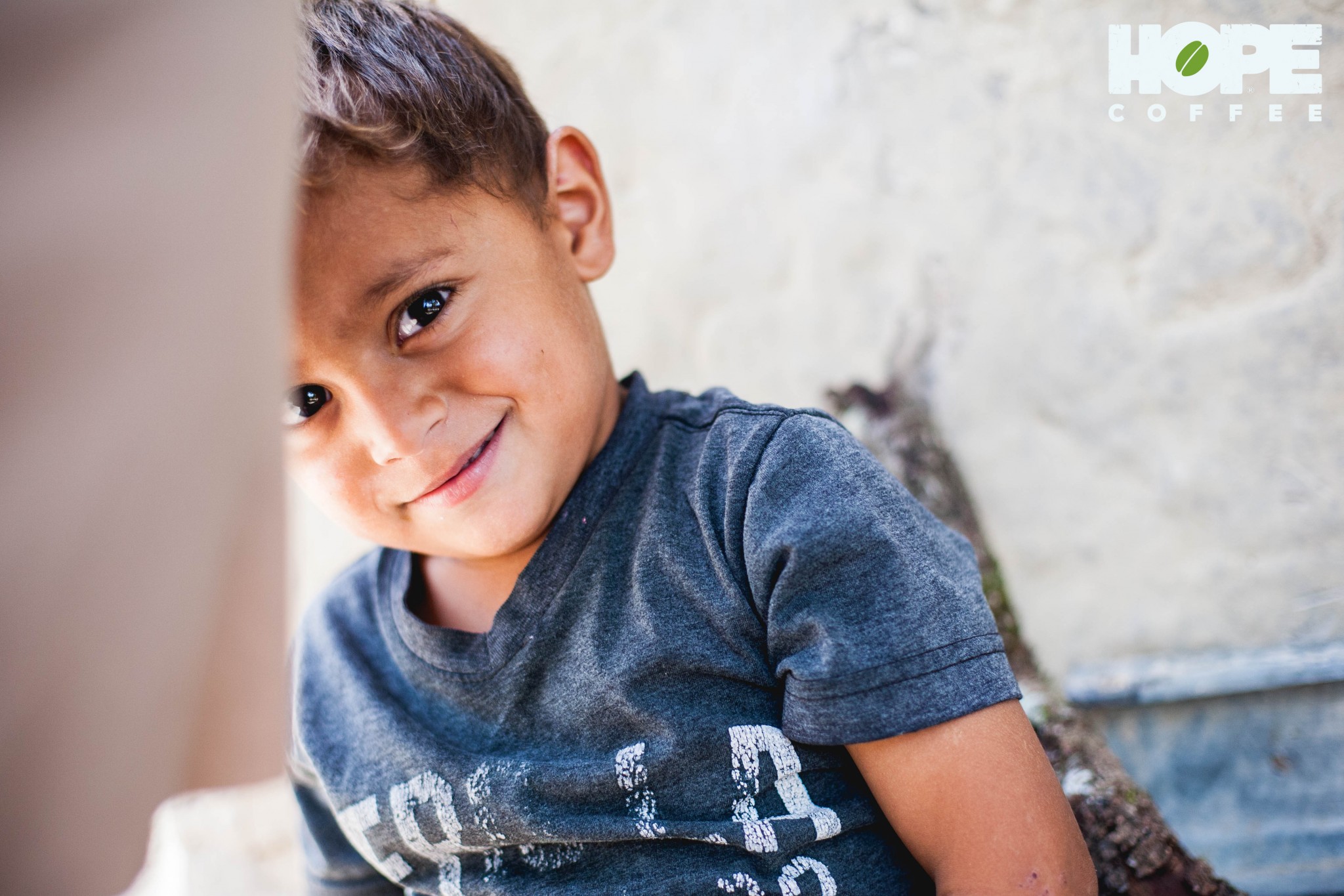 A playful 3-year-old boy smiles and hides behind his mom as she talks about the many needs her family faces. His family needs a new roof on their mudbrick home.